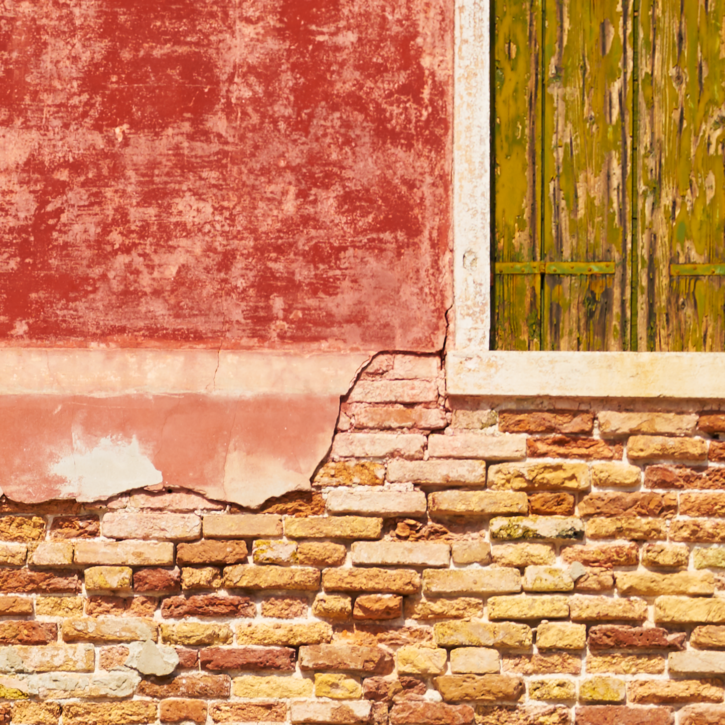 Worn brick wall with peeling paint and a green shutter.