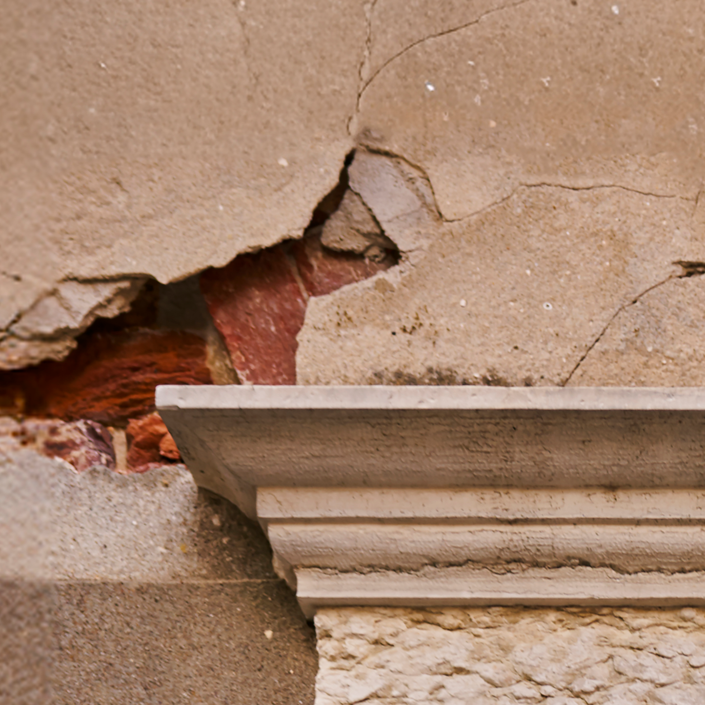 Close-up of a stone wall with a decorative cornice and a large crack.