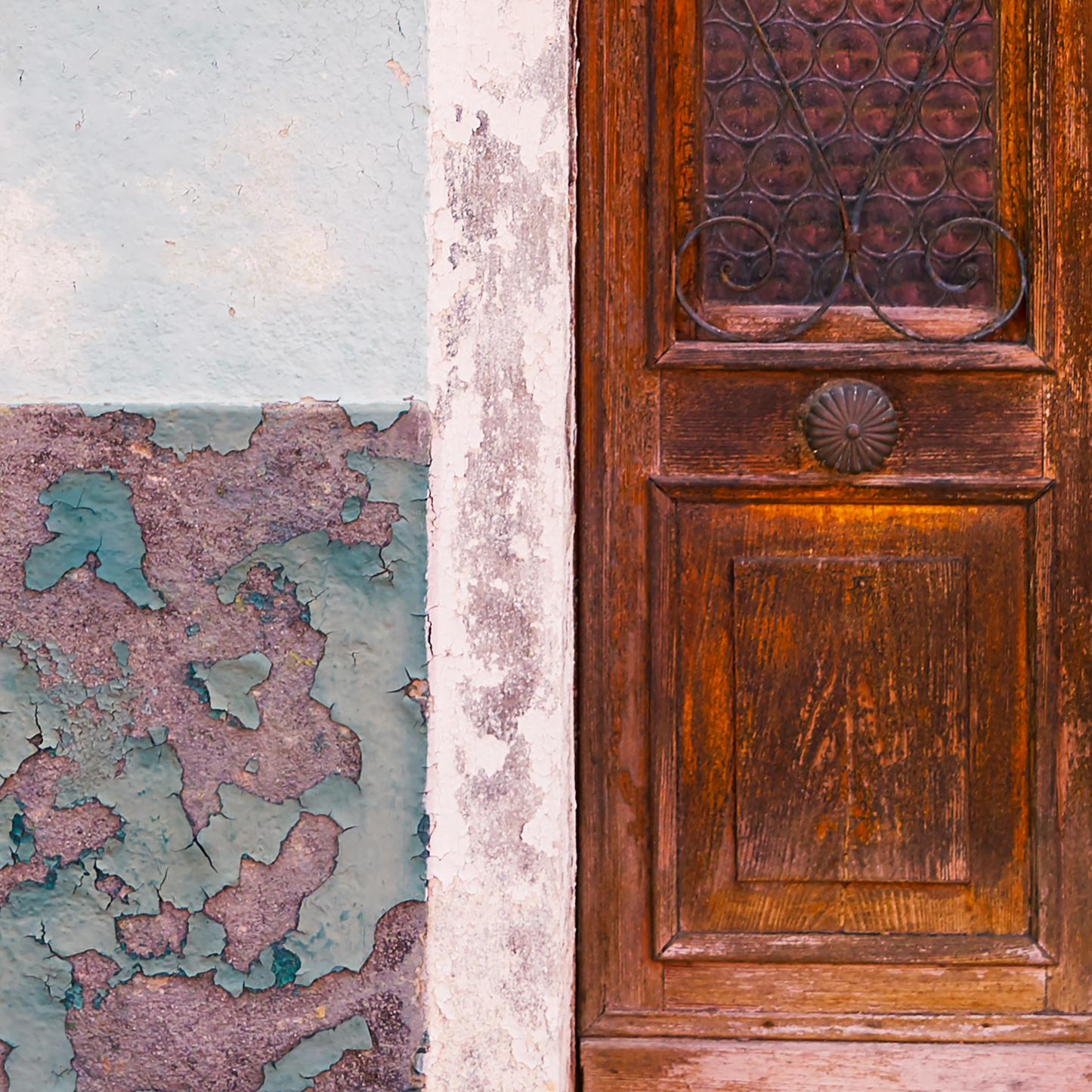 Close-up of a wooden door with decorative ironwork and peeling paint on a wall.