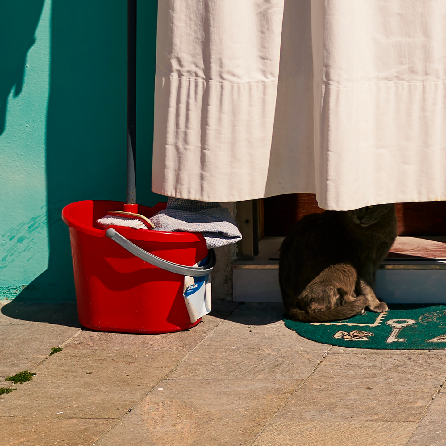 Red bucket with clothes on a stone floor next to a white curtain.