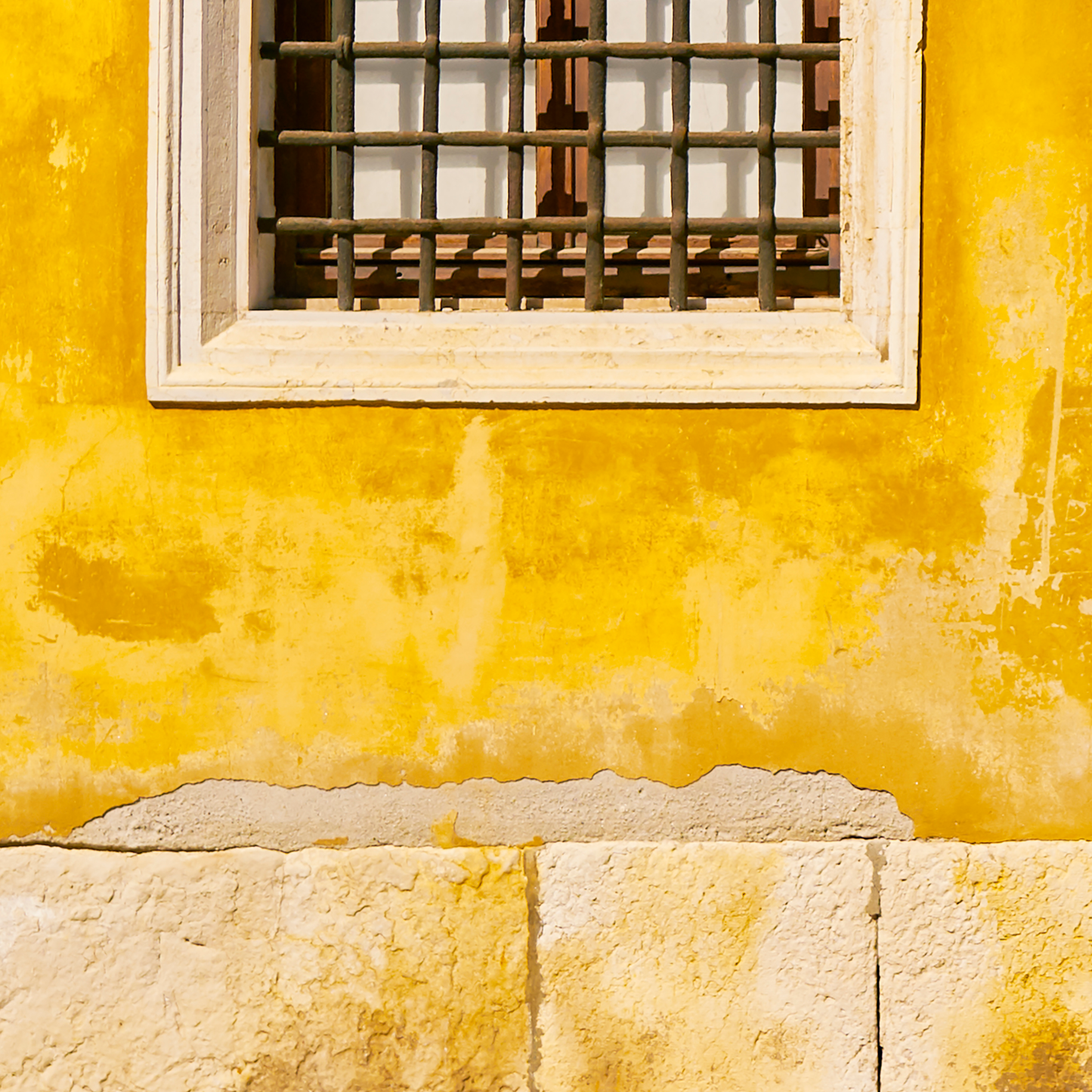 Yellow wall with a window featuring a metal grille.