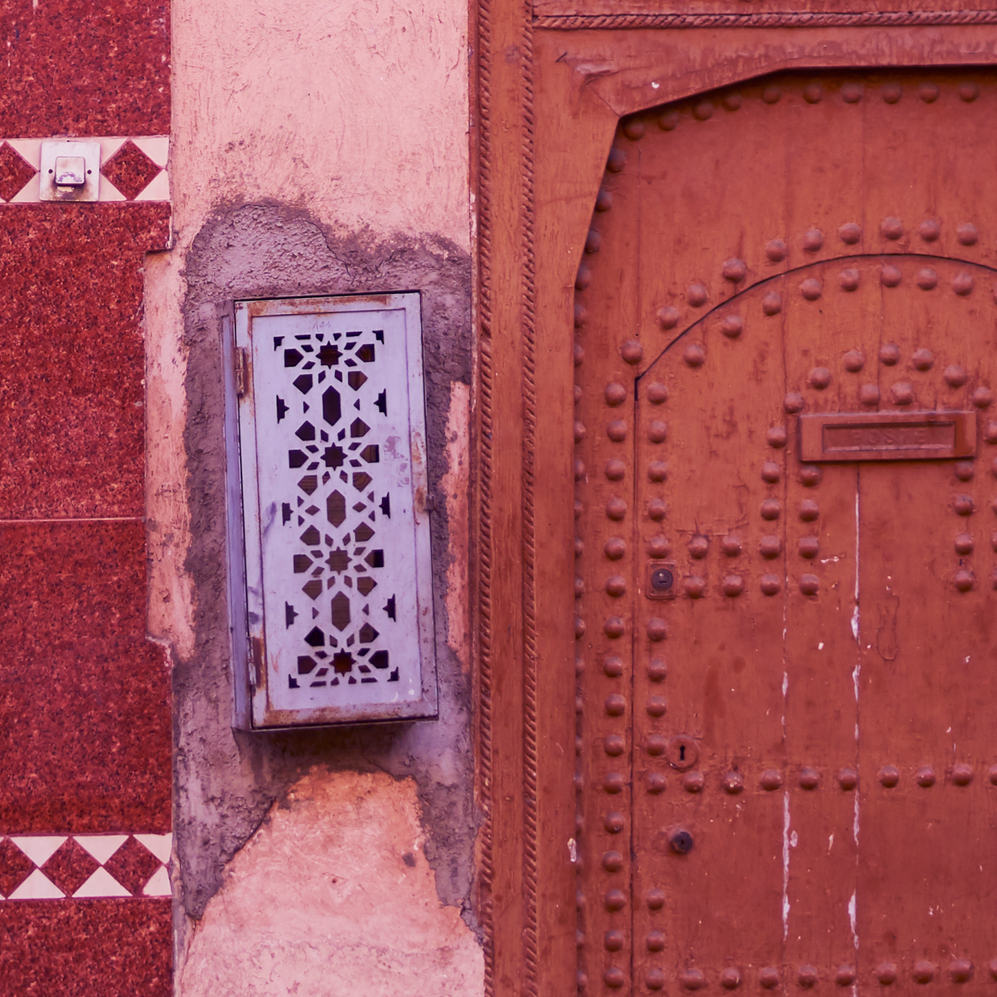 Decorative metal grille on a red wall with an ornate wooden door.