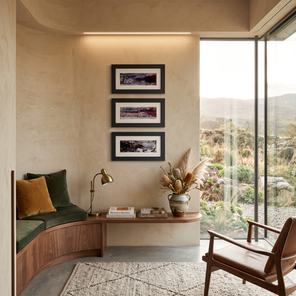 A styled interior corner with a curved wooden bench, green cushions, a wall-mounted wooden shelf, framed abstract prints on the wall, a brass desk lamp, a ceramic vase with dried grasses, and a large glass sliding door overlooking an outdoor landscape. No person or animal is present.