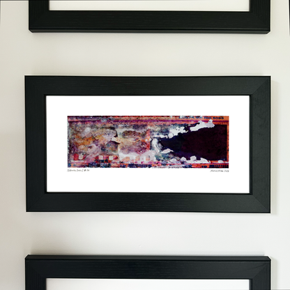 A framed abstract art print with a colorful textured design in red, purple, and white, set within a black frame and mounted on a light beige wall.