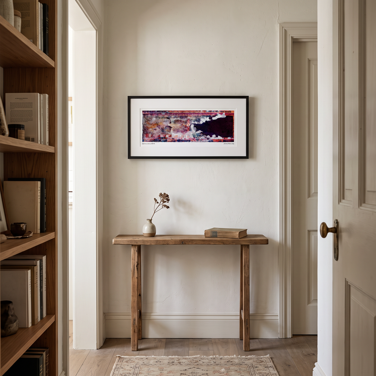 A framed abstract art print with a black frame and white mat hangs on a beige wall above a rustic wooden console table in a styled home entryway.