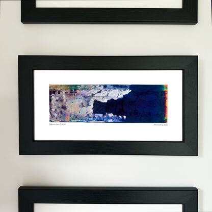 A framed abstract art print with a black frame and white mat, displayed on a light wall. The artwork features a dark blue textured area on the right with splashes of purple, pink, and green on the left.