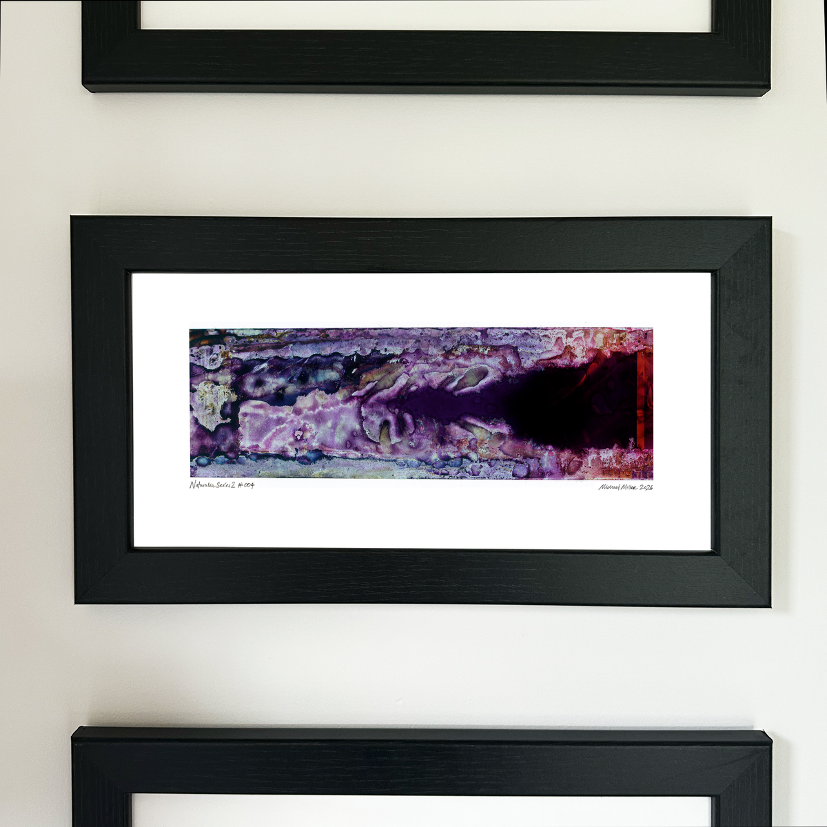 A framed abstract art print with a purple, black, and red pattern, mounted on a white wall between other black-framed prints.