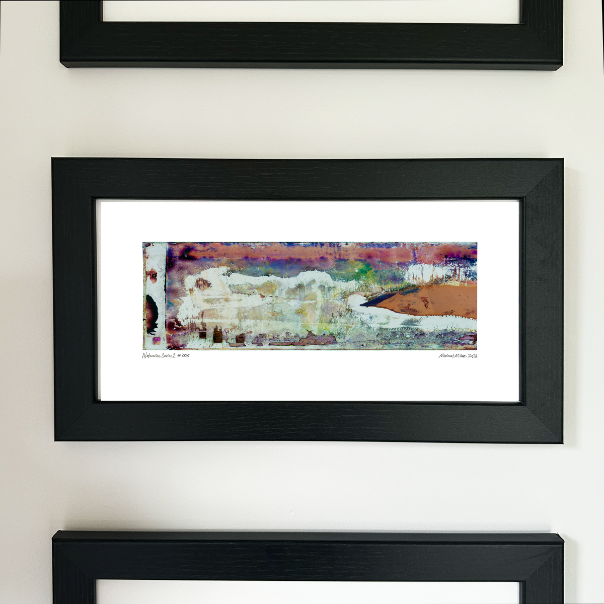 A framed abstract art print with a black frame and white mat, featuring Naturalia II #005 in peach, pink and green tones, mounted on a white wall.
