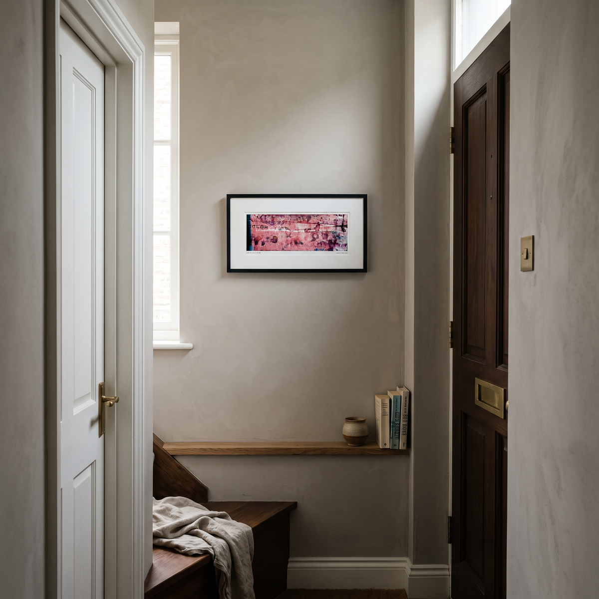 A framed panoramic abstract art print in pink, purple and black tones, displayed on a wall in a styled interior setting.

