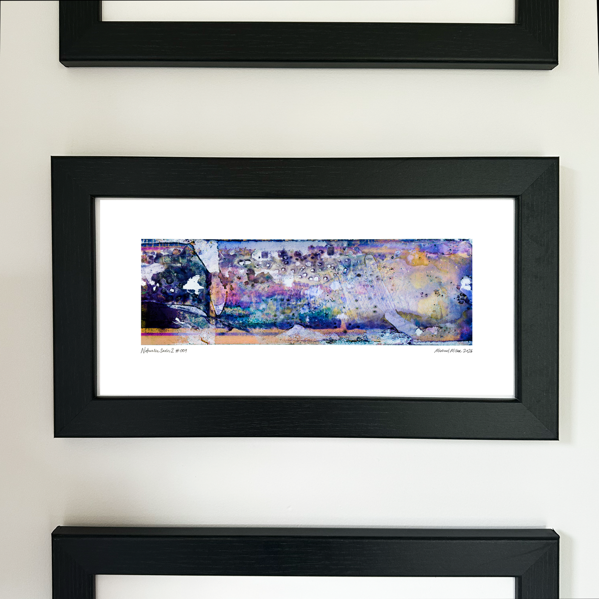 A framed abstract art print with a black frame and white mat, featuring Naturalia II #009 in blue, purple and peach tones, mounted on a white wall.
