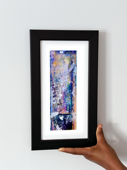 A hand holding a black-framed abstract art print with a white mat, featuring Naturalia II #009 against a plain white wall.
