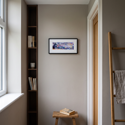 A framed panoramic abstract art print in blue, purple and peach tones, displayed on a wall in a styled interior setting.
