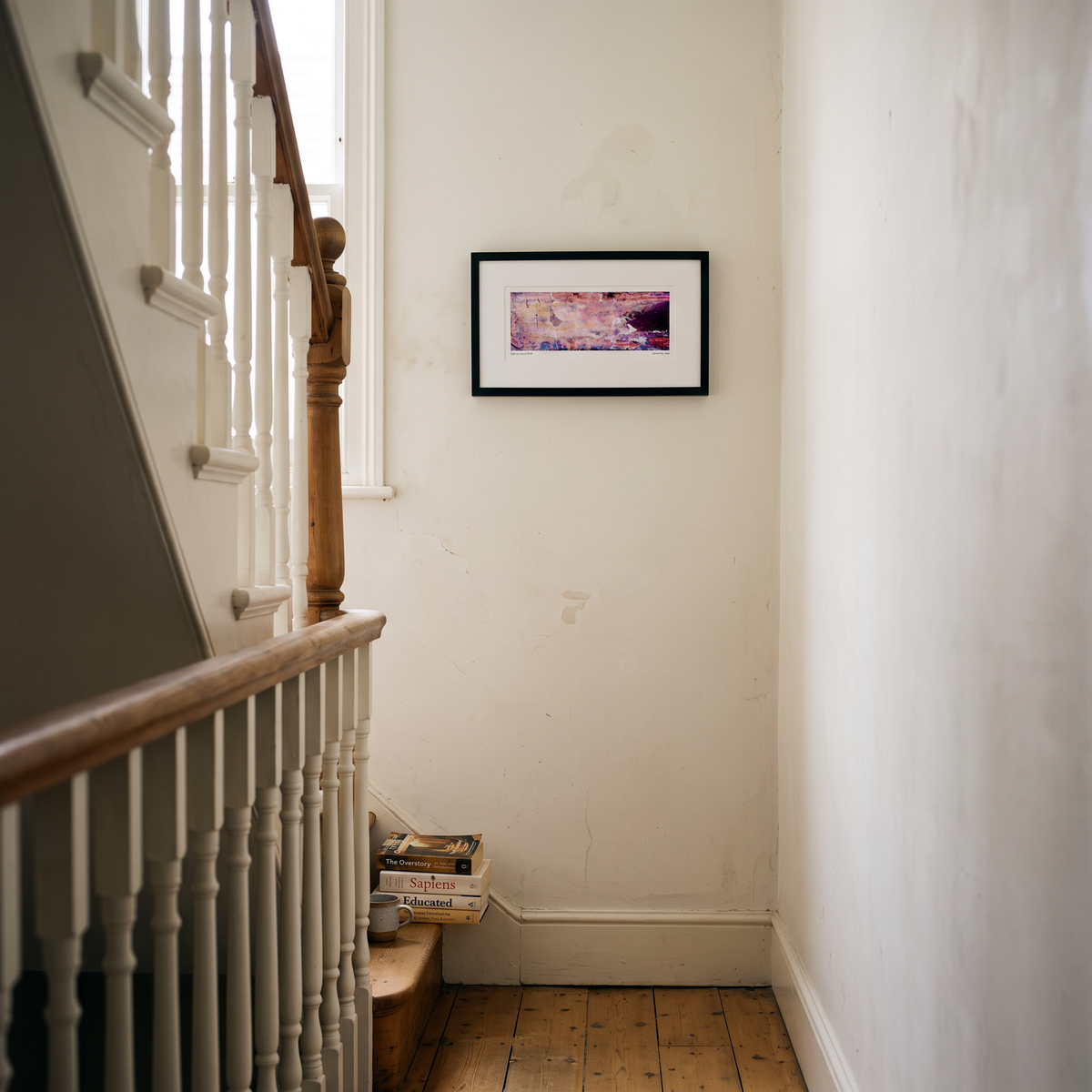 A framed panoramic abstract art print in pink, peach, purple and blue tones, displayed on a wall in a styled interior setting.
