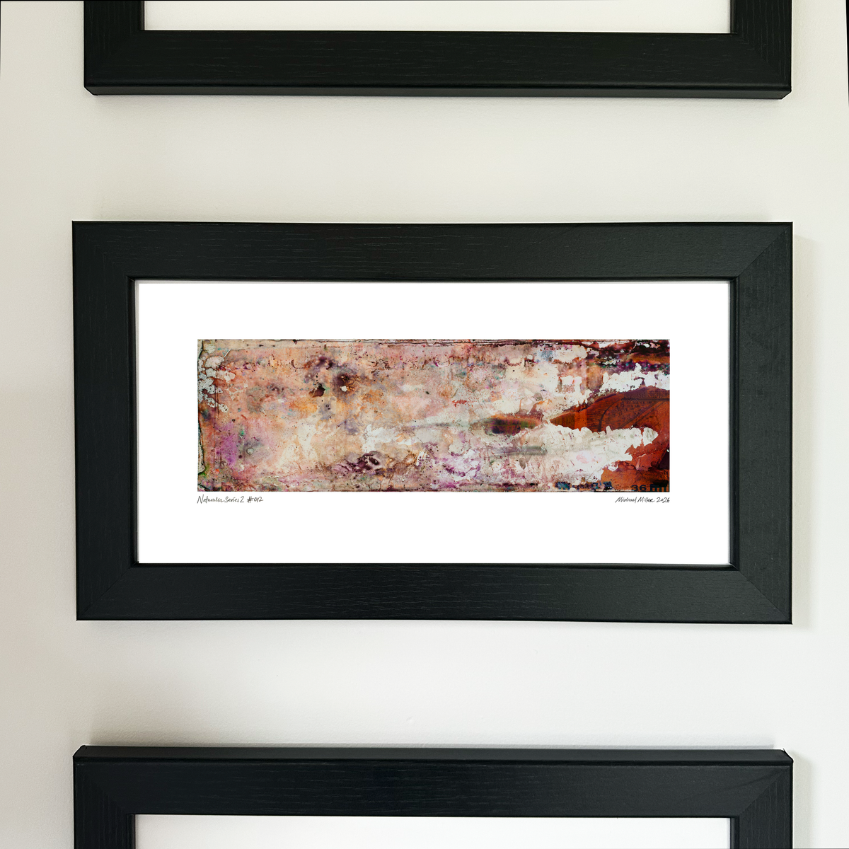 A framed abstract art print with a black frame and white mat, featuring Naturalia II #012 in pink, peach and orange tones, mounted on a white wall.
