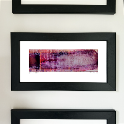 A framed abstract art print with a black frame and white mat, featuring Naturalia II #015 in pink, purple and burgundy tones, mounted on a white wall.
