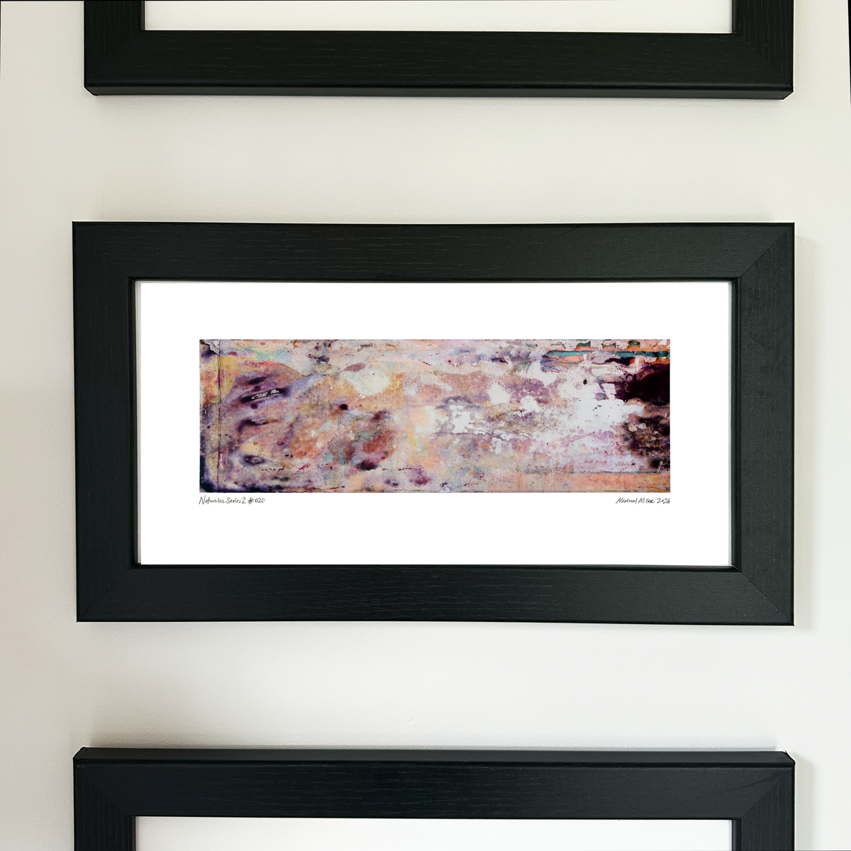 A framed abstract art print with a black frame and white mat, featuring Naturalia II #020 in soft peach and lavender tones, mounted on a white wall.
