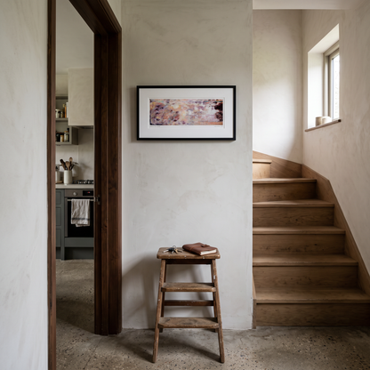 A framed panoramic abstract art print in soft peach and lavender tones, displayed on a wall in a styled interior setting.
