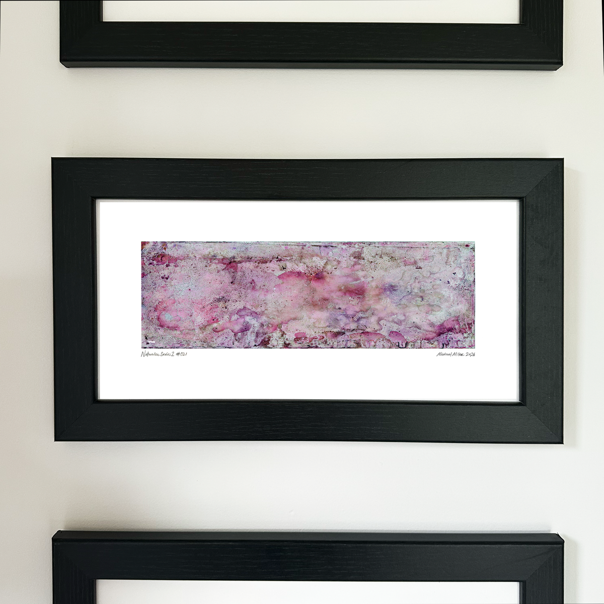 A framed abstract art print with a black frame and white mat, featuring Naturalia II #021 in delicate pink and lavender tones, mounted on a white wall.
