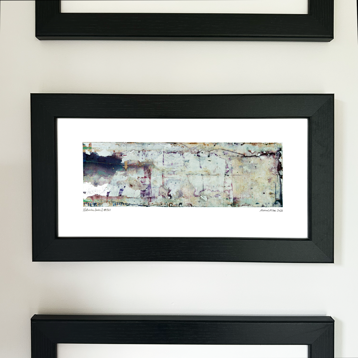 A framed abstract art print with a black frame and white mat, featuring Naturalia II #023 in cream, pale blue and lavender tones, mounted on a white wall.
