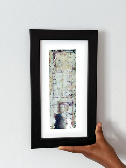 A hand holding a black-framed abstract art print with a white mat, featuring Naturalia II #023 against a plain white wall.
