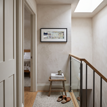 A framed panoramic abstract art print in cream, pale blue and lavender tones, displayed on a wall in a styled interior setting.
