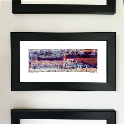 A framed abstract art print with a black frame and white mat, featuring Naturalia II #024 in purple, pink and orange tones, mounted on a white wall.
