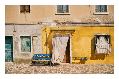 Colorful building facade with a bench and hanging curtains in a sunlit street in Venice Italy