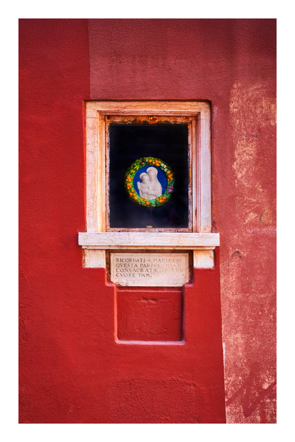 Small window with decorative plaque on a red wall in Venice Italy