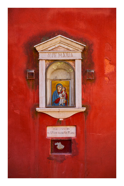 Small religious shrine with an icon of a woman and child on a red wall in Venice Italy