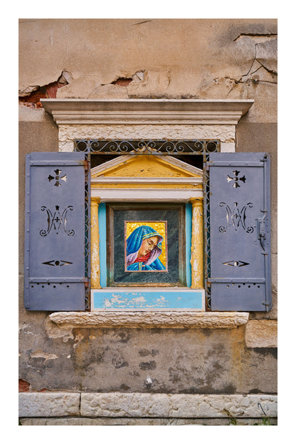 Decorative window with a religious icon and blue shutters on an old building in Venice Italy