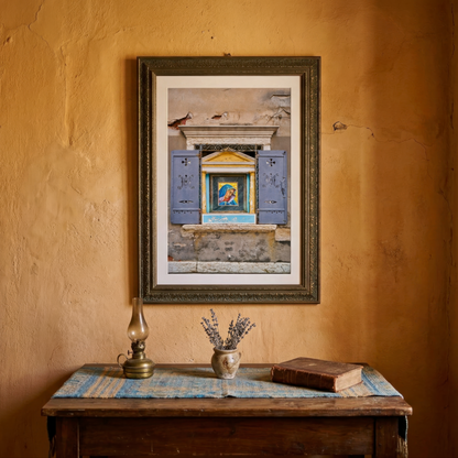 Framed photograph of a religious home made shrine on a wall in Venice, on a wall above a wooden table with a lamp and books. 