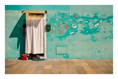 Shuttered door with a curtain against a textured teal wall in Venice Italy