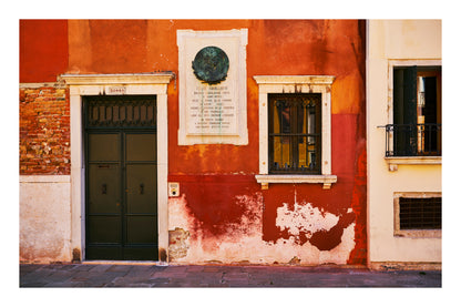 Red building facade with a door, window, and plaque in Venice Italy