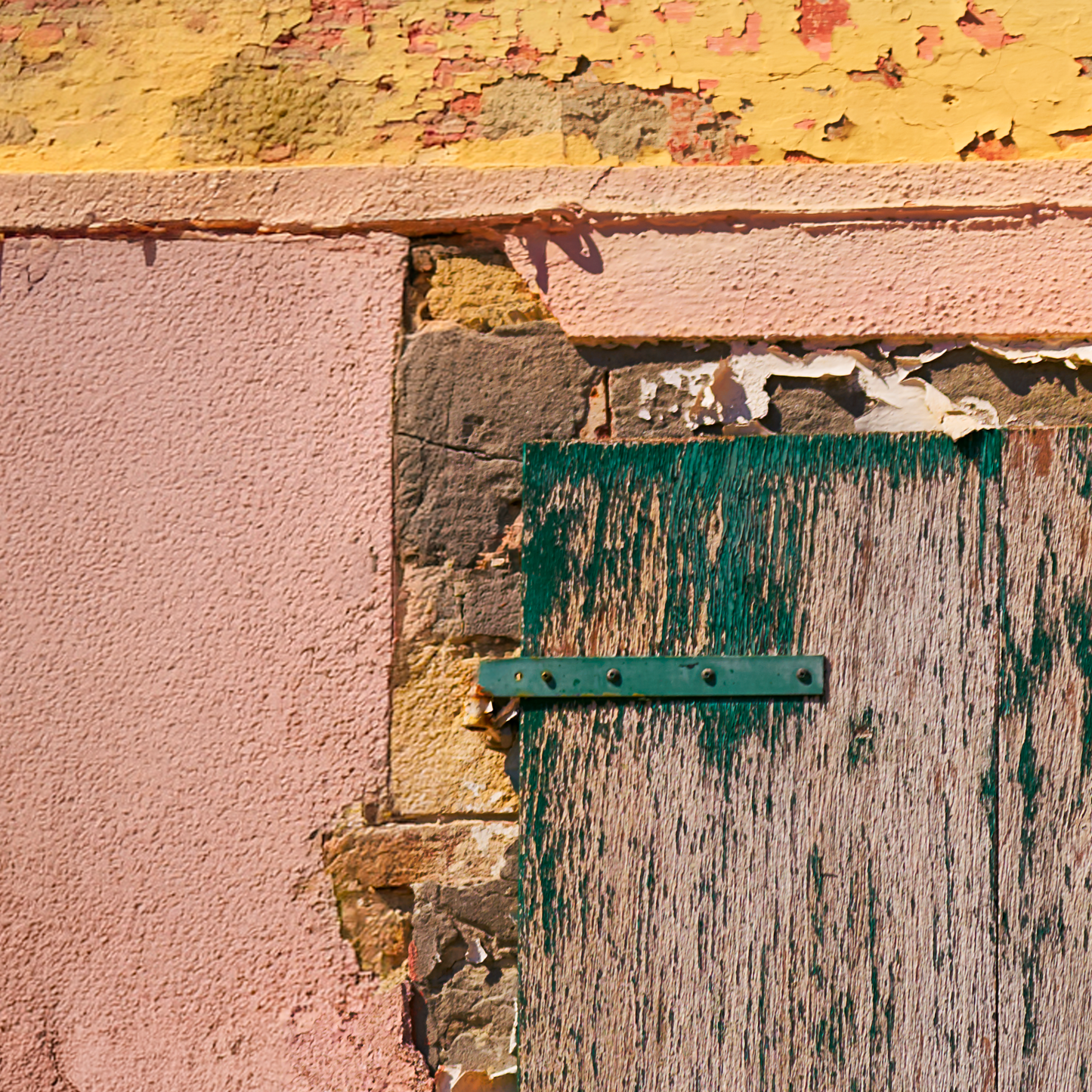 Close-up of a textured wall with peeling paint and a green metal bracket.
