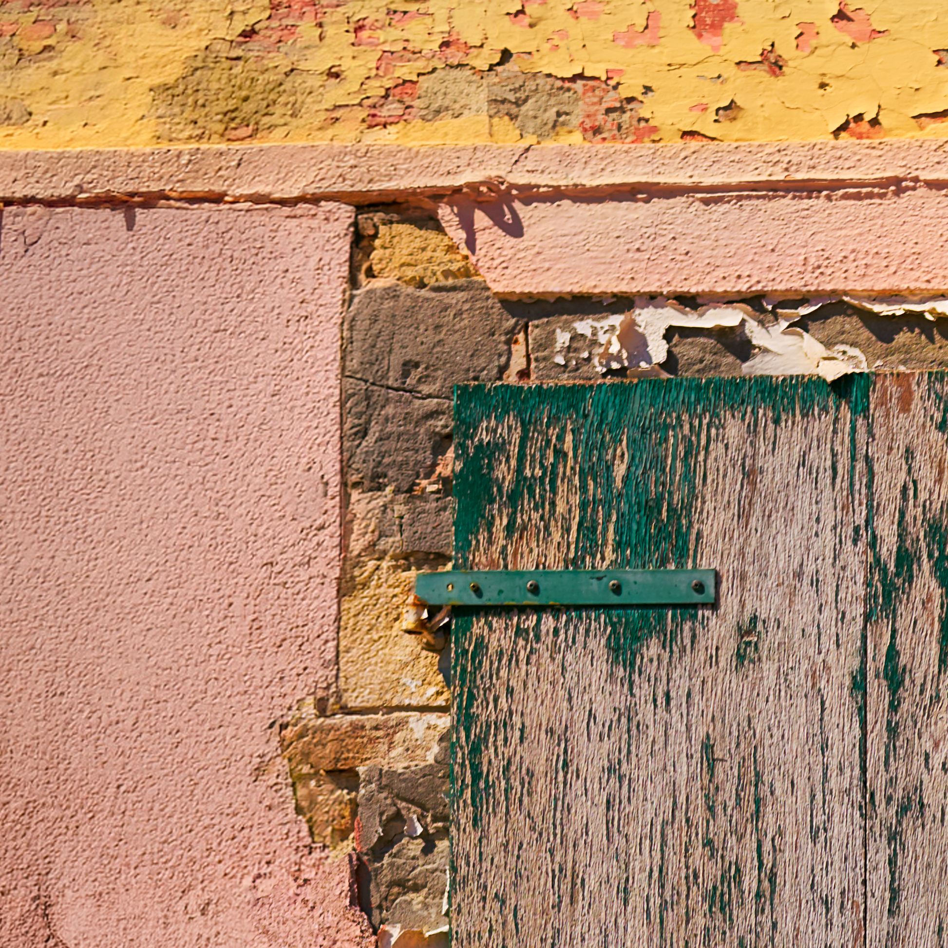 Close-up of a textured wall with peeling paint and a green metal bracket.