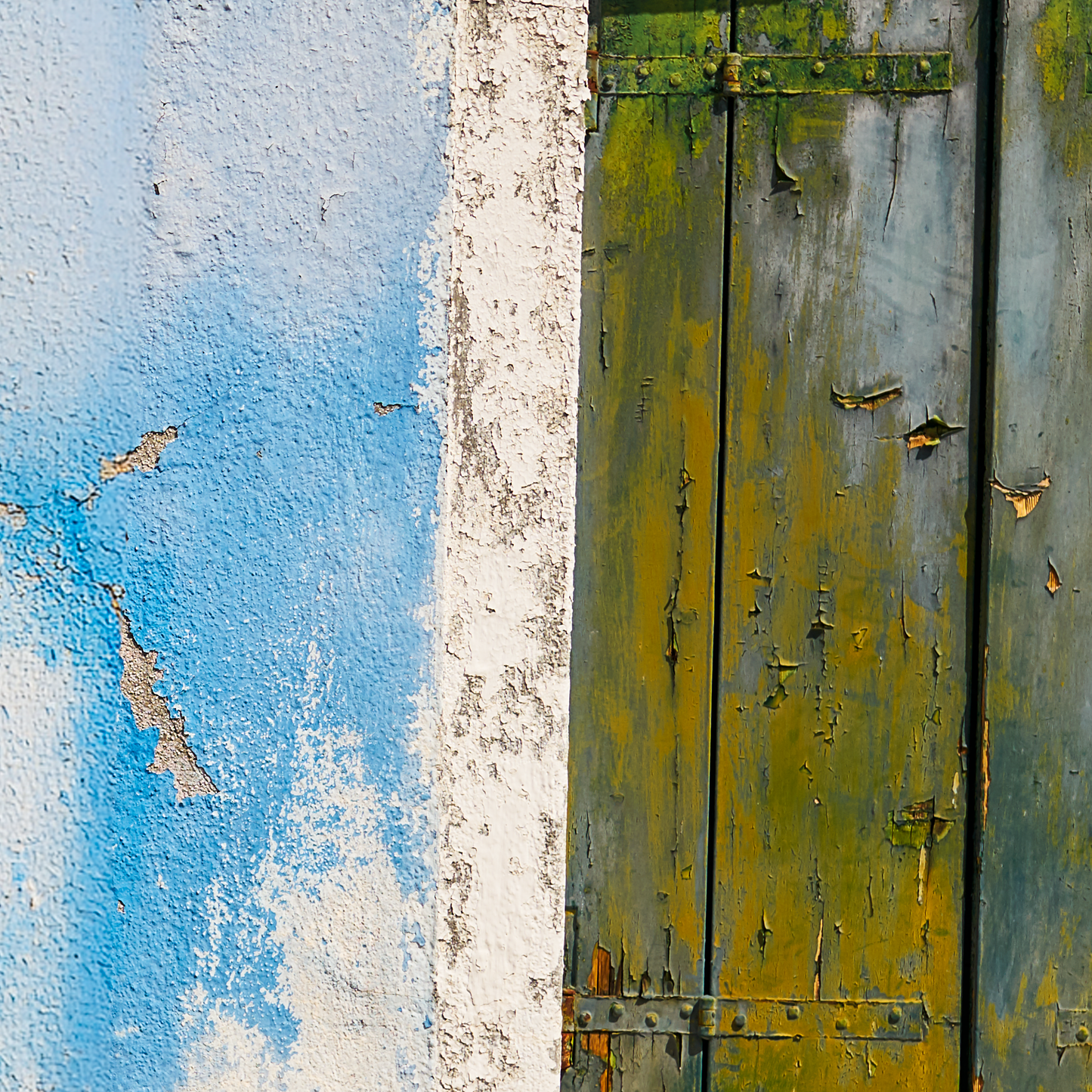 Rustic wooden door with peeling paint next to a blue wall.