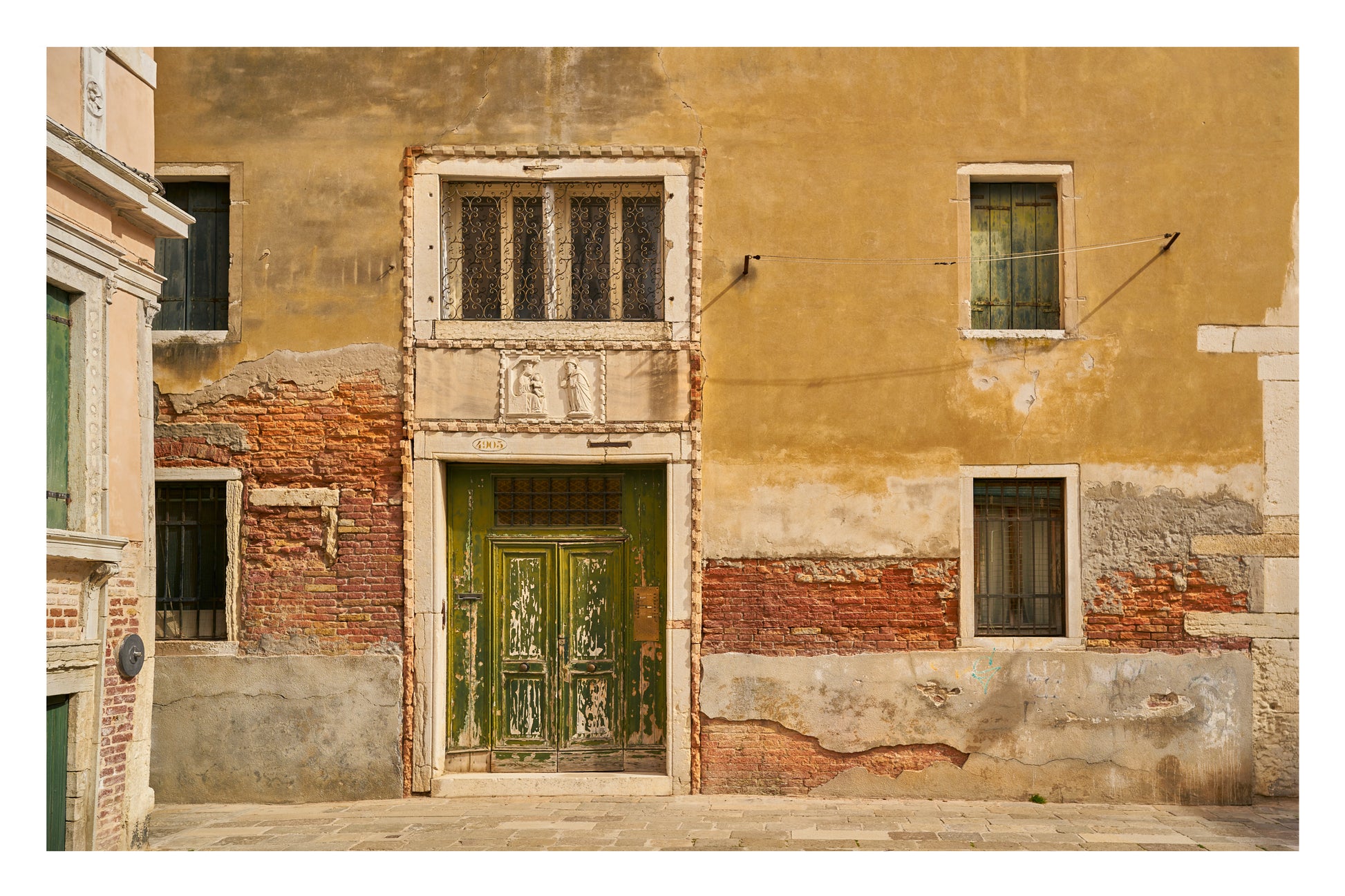 Worn-out building facade with a green door and windows in Venice