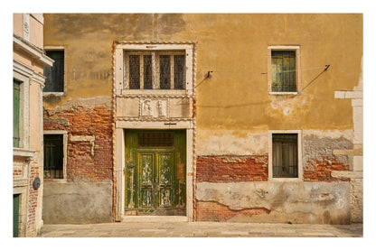 Worn-out building facade with a green door and windows in Venice