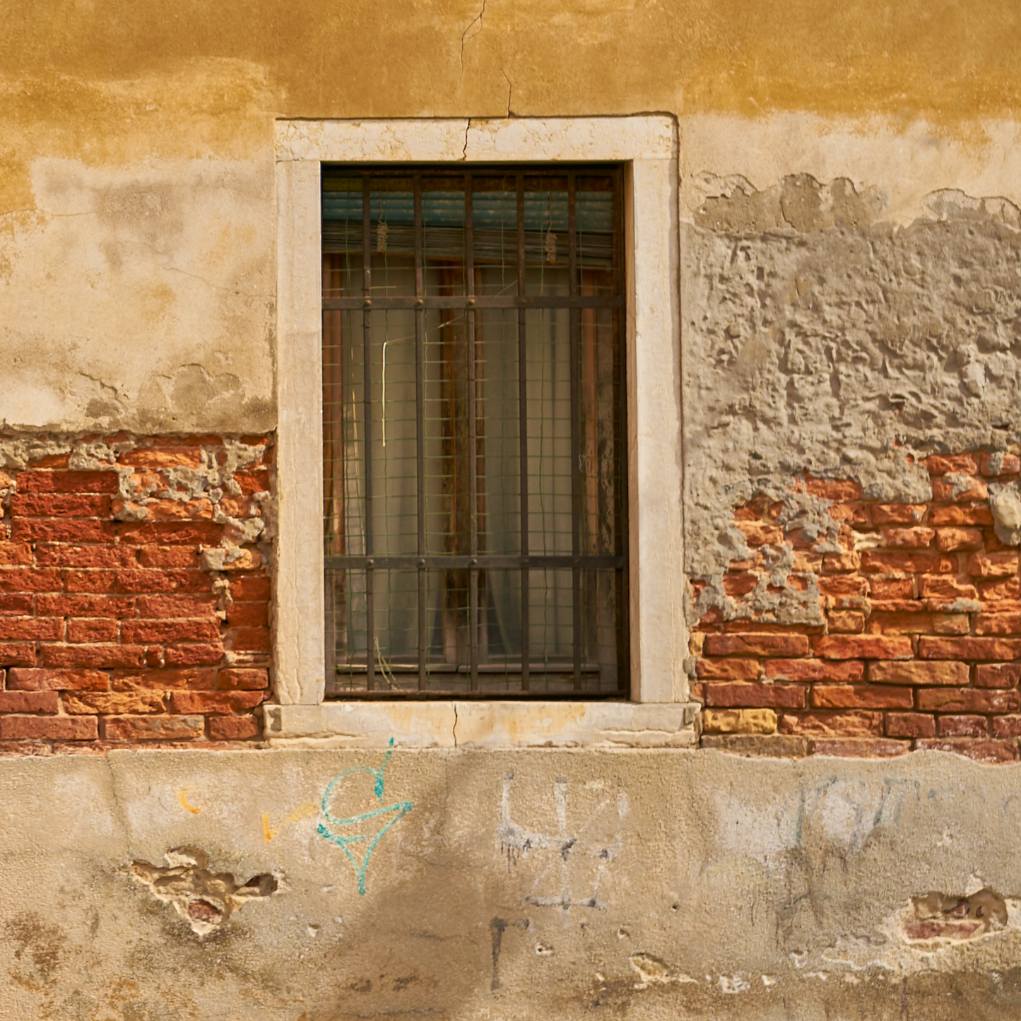 Window with bars on a textured wall with visible wear and graffiti.