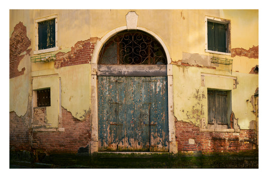 Old, weathered building facade with a large door and windows showing signs of decay.