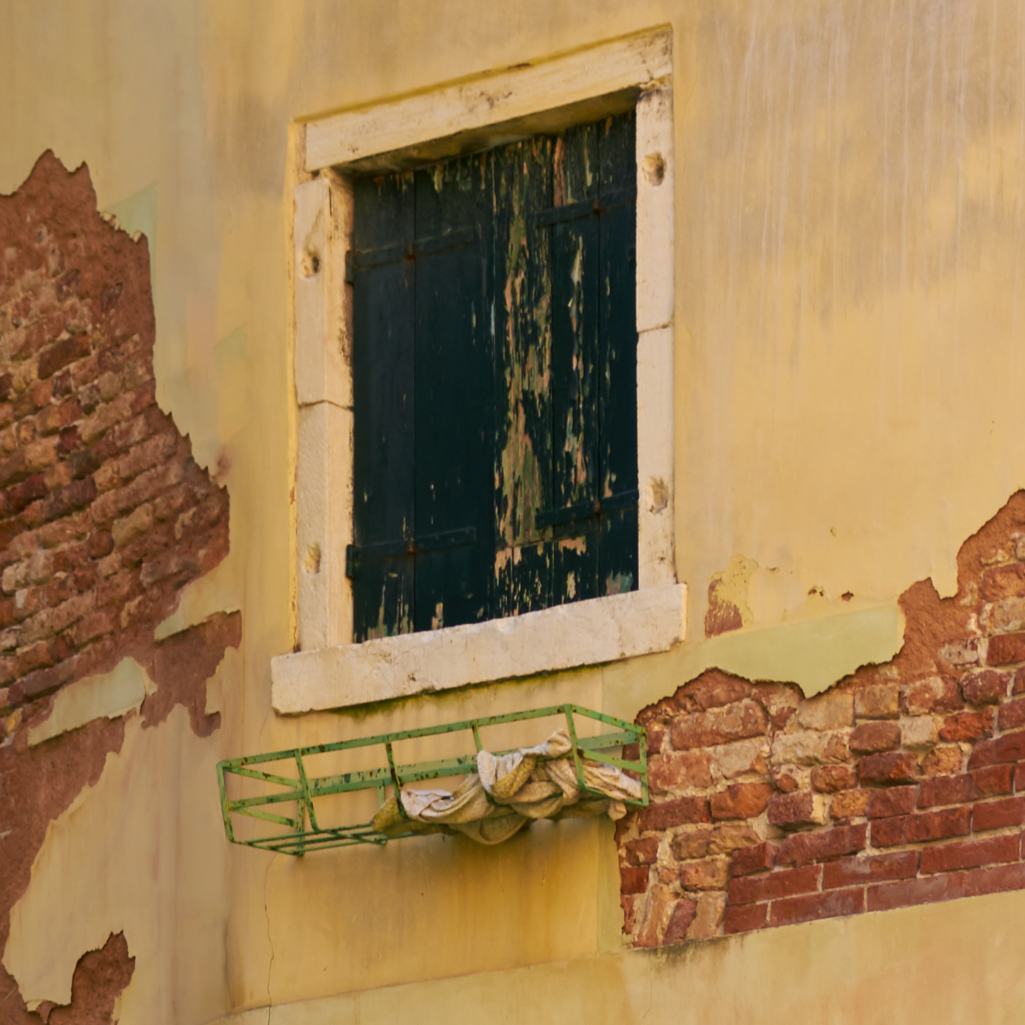 Worn-out wall with a window and a green metal shelf.