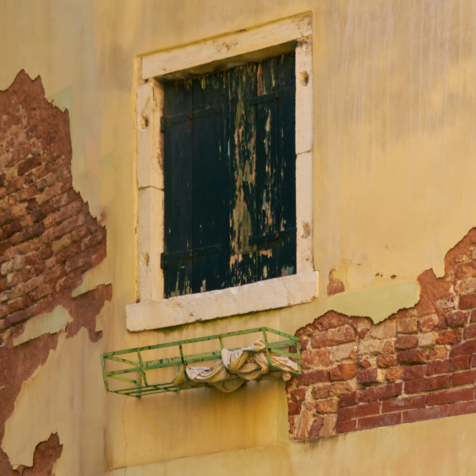 Worn-out wall with a window and a green metal shelf.