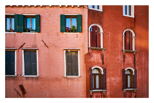 Red brick building with green shutters and arched windows in Venice, Italy.