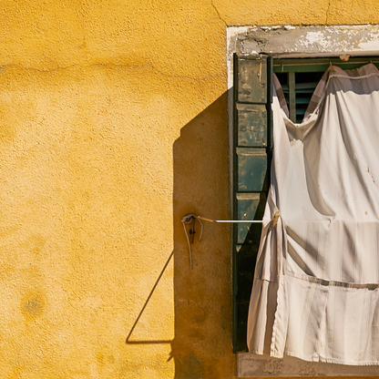 Window with white curtain on a yellow wall
