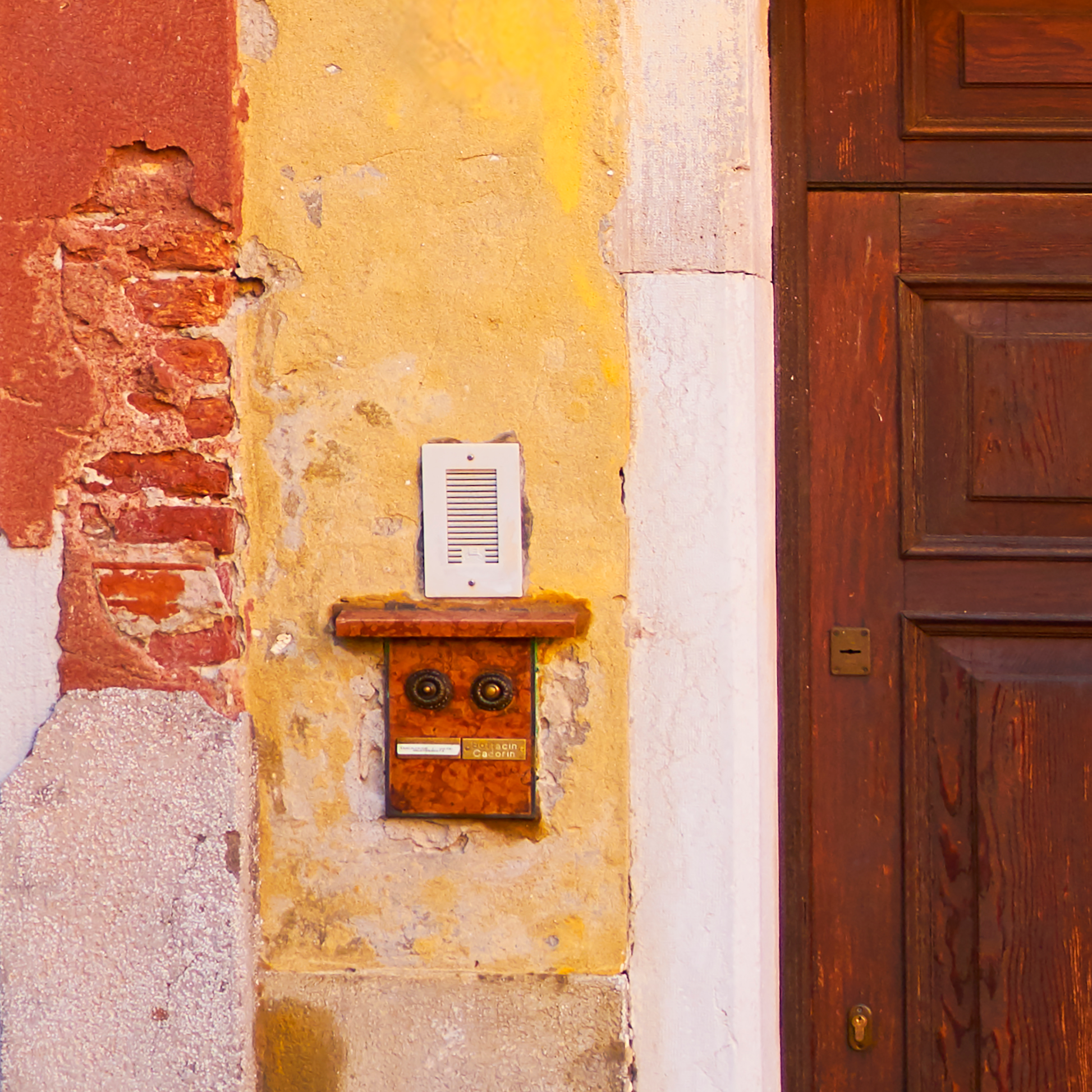 Vintage doorbell on a textured wall with a wooden door.