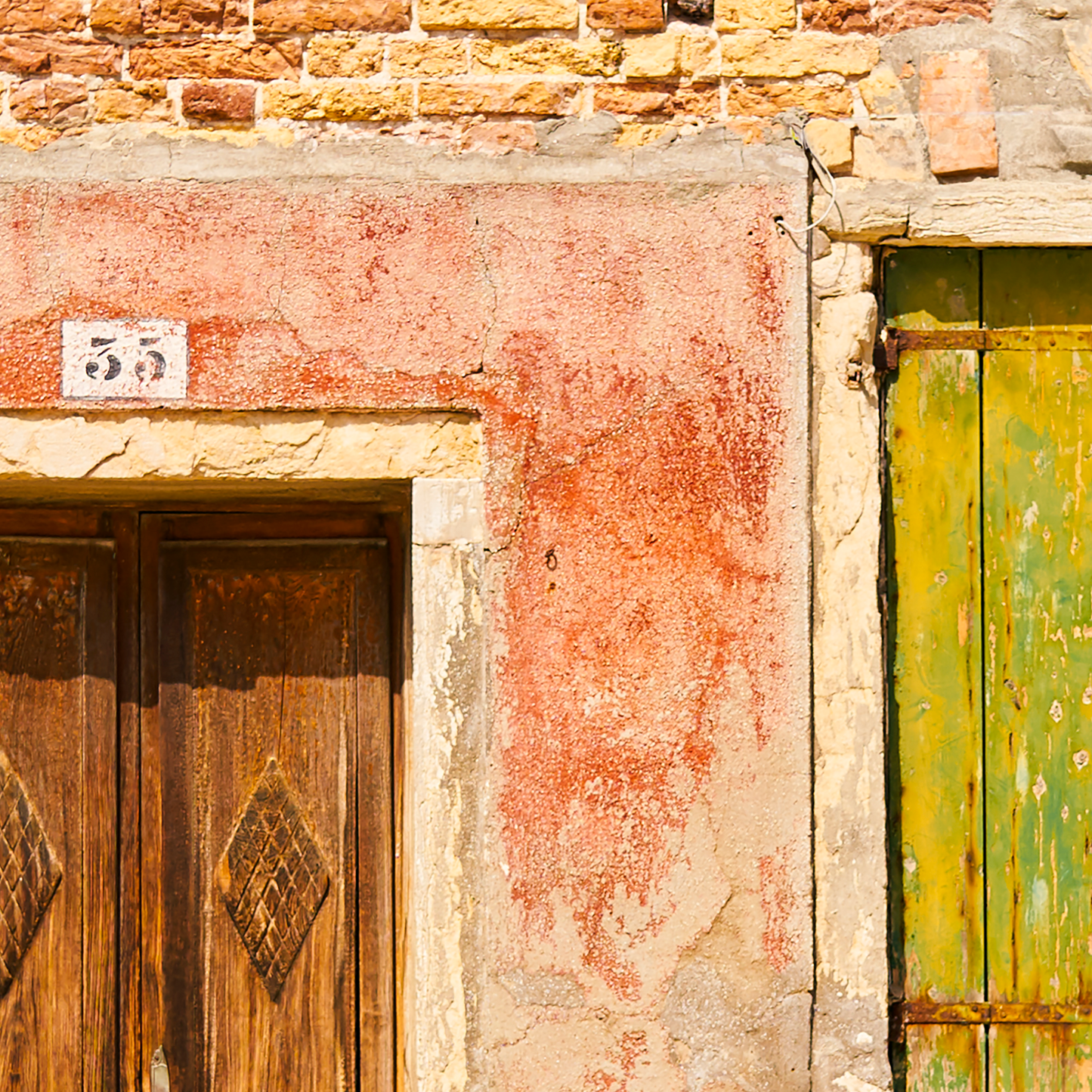 Close-up of a rustic building facade with wooden door and green shutter.