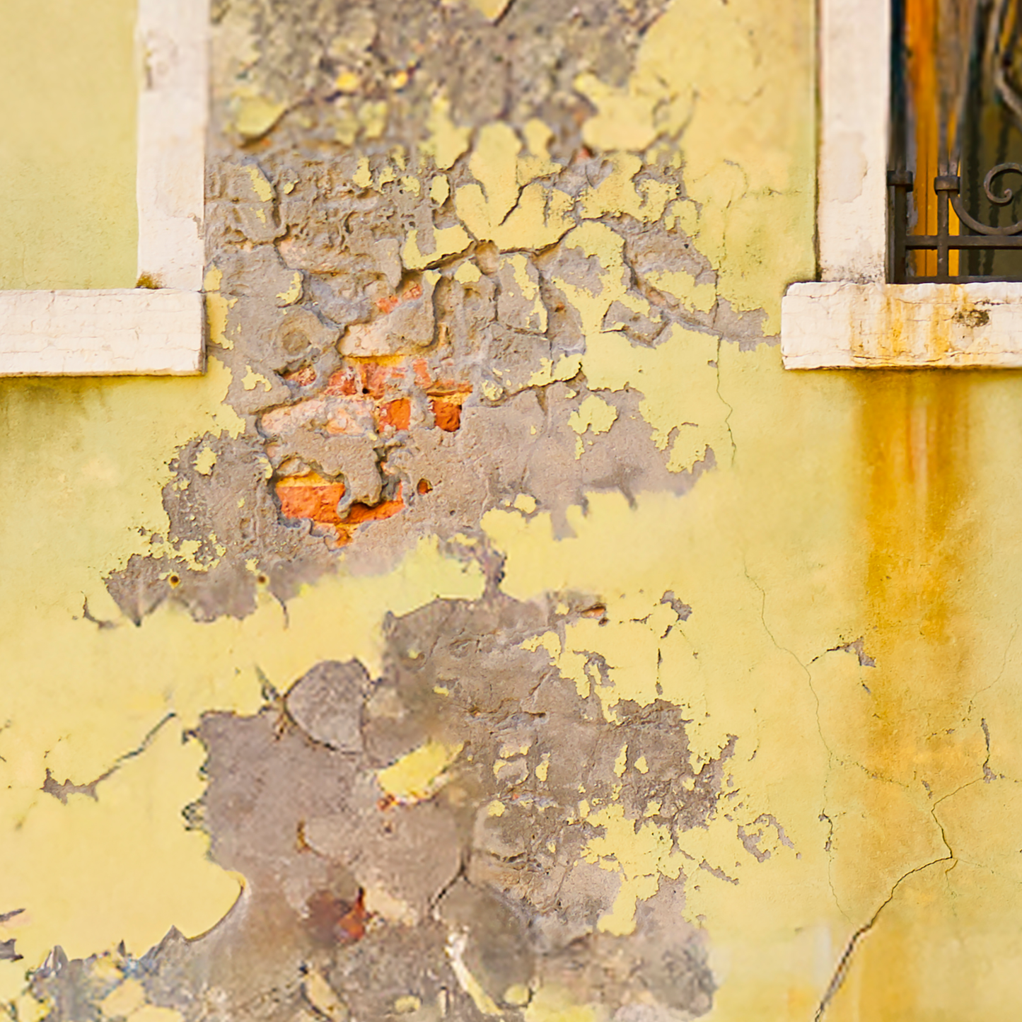 Peeling paint on a yellow wall with a window frame.