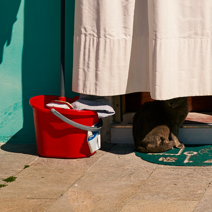 Red bucket with clothes on a stone floor next to a white curtain.