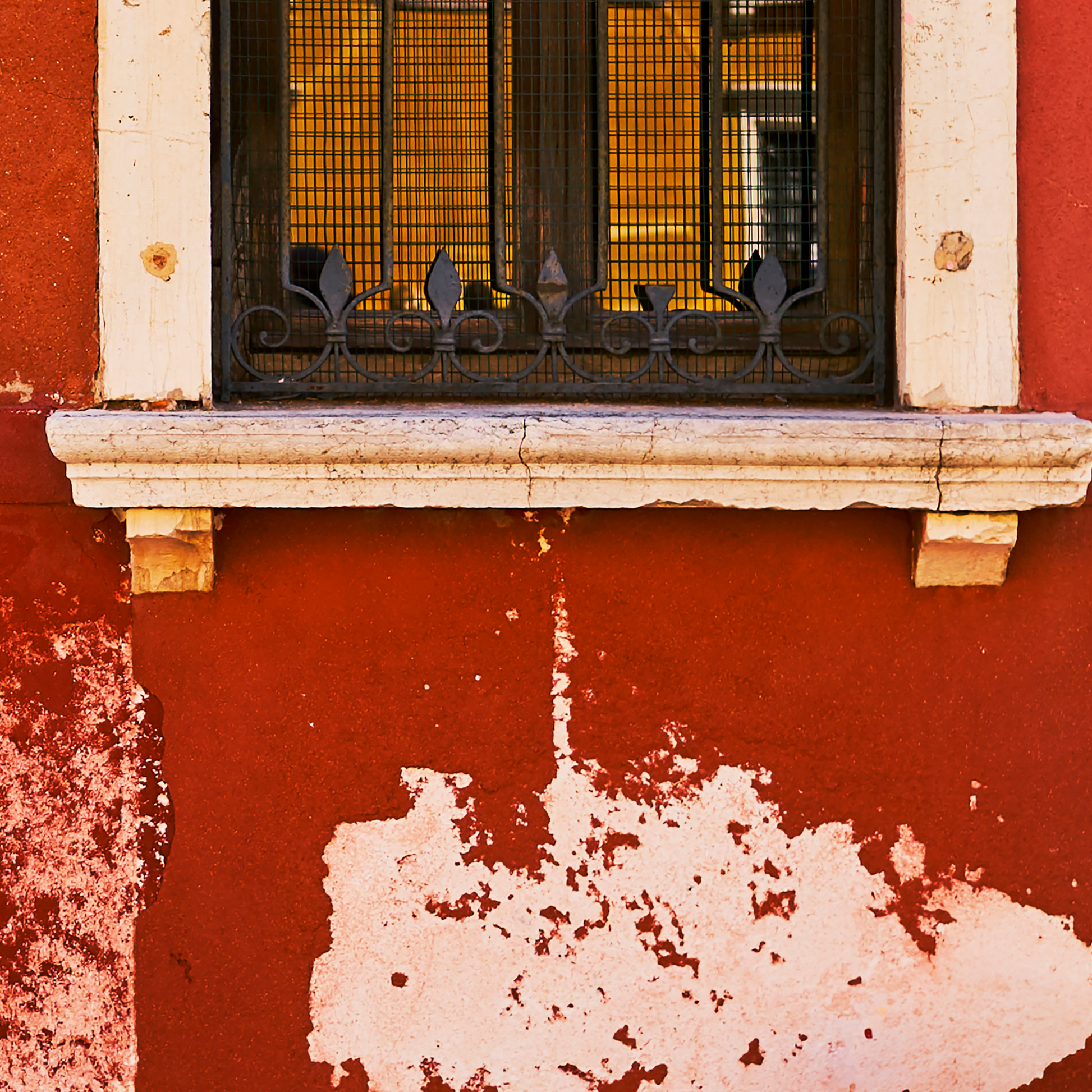 Window with decorative grille on a red wall with peeling paint