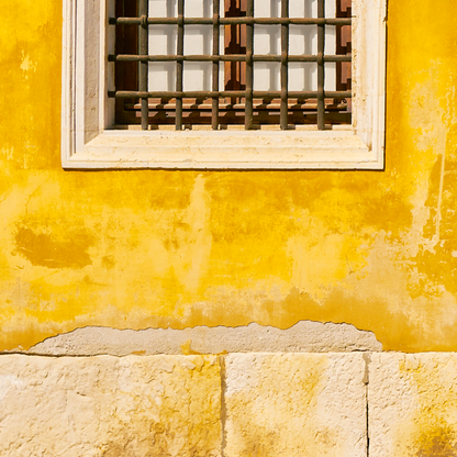 Yellow wall with a window featuring a metal grille.